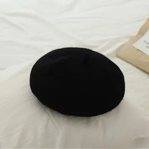 Detail view of a classic black wool beret hat for girls on a soft fabric background