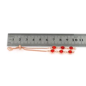 Détail d'un bracelet réglable en or rose avec cristaux rouges à côté d'une règle