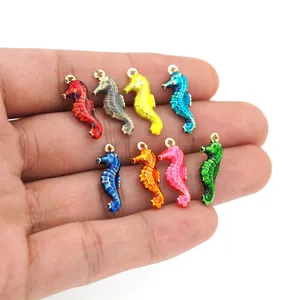 Détail de huit pendentifs hippocampe colorés plaqués or 18 carats présentés dans la main