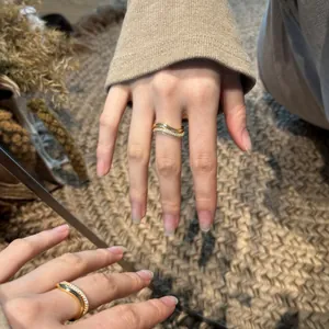 Detail of gold double-layered wavy ring with white cubic zirconia on a model's finger