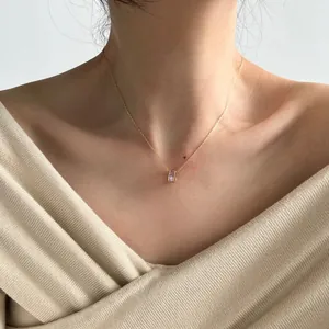 Detail of gold necklace with cylindrical pendant featuring baguette-cut pink zircons on model