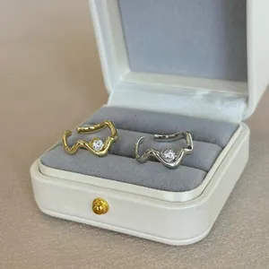 Detail view of gold and silver wavy rings with round zircon in a beige jewelry box