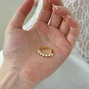 Close-up of gold ring with seven white pearls held in hand on white lace background