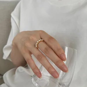 Close-up of elegant gold ring set with white pearls worn on finger holding a glass