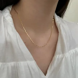 Detalle de un collar minimalista de cadena ondulada dorada usado en la clavícula con luz suave