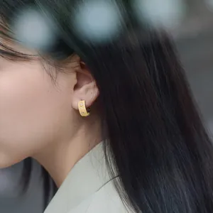 Close-up of brushed gold hoop earring with two inset clear zircons on model