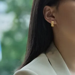 Detail of brushed gold hoop earring with two inlaid zircons worn by a model