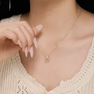 Gold octagon pendant necklace with sparkling letter A charm on a white lace shirt