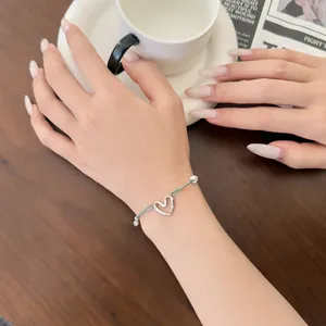 Bracelet en corde tressée gris-vert avec breloque cœur évidé en argent sterling S925 au poignet
