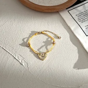 Dettaglio macro del bracciale in corda gialla intrecciata con cuore dorato e pietra zircone