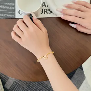 Détail d'un bracelet doré avec cœur évidé et zircon sur une main sur table en bois