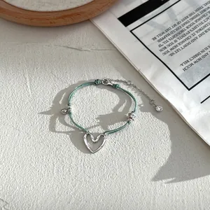 Dettaglio del bracciale intrecciato verde con ciondolo a cuore e piccoli cristalli lucidi