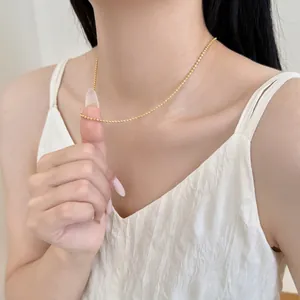 Dettaglio della collana a sfere dorate minimalista indossata da una modella elegante