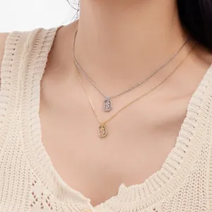 Close-up of gold and silver S-letter pendants with micro-pave crystals on a model