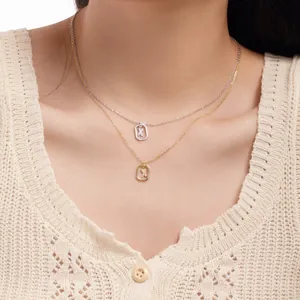 Close-up of layered silver and gold necklaces with square diamond letter X pendants