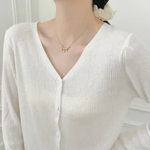 Detail of a gold water-drop pendant necklace with metal beads on a V-neck sweater