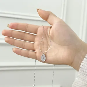 Detailed close-up of a silver oval pendant with radial pattern and small zircon stone