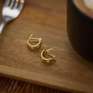 Detailed macro of golden C-shaped earrings with sunburst zircon inlays and matte finish