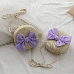Dettaglio borsa tonda in paglia con grande fiocco viola a pois e tracolla in cotone