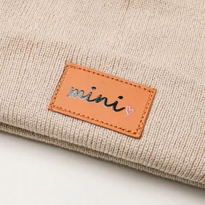 Gebreide kindermuts met dubbele pompons en een mini-hartje leren label detail