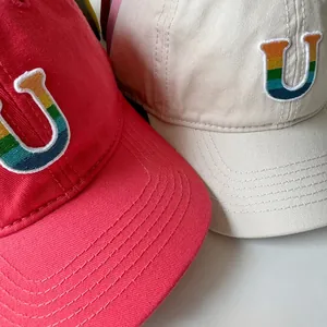 Détail de la broderie lettre U arc-en-ciel sur casquettes de baseball en coton rouge et beige