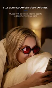 Woman in bed wearing blue light blocking glasses with red lenses and gold detail