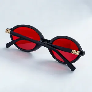 Detail of oval sunglasses with black frames, red lenses and gold metallic accents