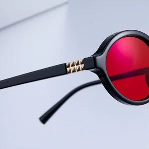 Detailed close-up of golden pyramid metal hinge on black oval sunglasses with red lenses