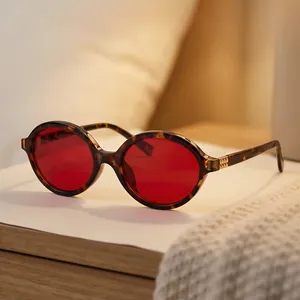 Vintage oval sunglasses with red lenses and tortoiseshell frame on a wooden surface