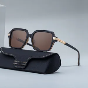 Lunettes de soleil carrées noires avec verres bruns et branches dorées sur étui en cuir