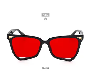Dettaglio frontale di occhiali da sole cat-eye neri con lenti rosse e accenti dorati