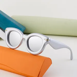 Silver cat eye sunglasses with thick matte frames and reflective lenses on orange case