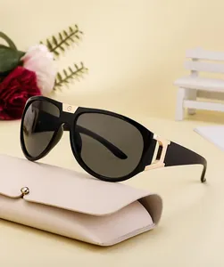 Detail of black aviator sunglasses with gold metal bridge and leather case on beige background