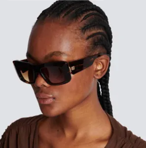 Detail of tortoiseshell square sunglasses with brown lenses and metal hinge logo on model
