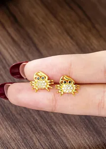 Detailed view of crab stud earrings in gold with white crystals held on fingertips