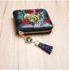 Détail du portefeuille en cuir noir avec gaufrage floral, pompon violet et zip cristal