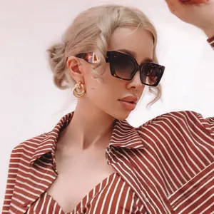 Close-up of tortoise shell square sunglasses with triangle metal detail and gold earrings