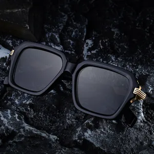 Quadratische schwarze Sonnenbrille mit goldenen Akzenten auf strukturiertem Mineralstein