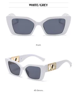 Detail view of white cat-eye sunglasses with gold V-shaped crystal logo on temple