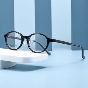 Modieus ovaal optisch brilmontuur in zwart met matgrijze poten op een blauwe standaard