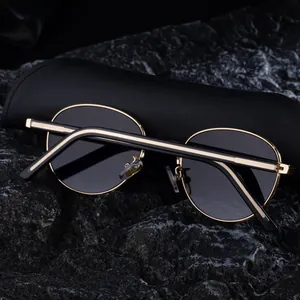 Detail van ovale zonnebril met goudkleurig montuur en luxe leren vouwkoker op steen