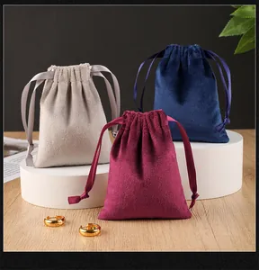 Macro view of velvet jewelry gift pouches in grey, navy, and maroon with ribbon drawstrings