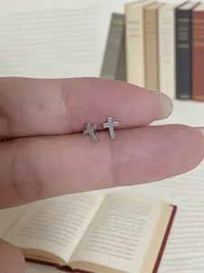 Close-up of small 925 sterling silver cross stud earrings held between fingers