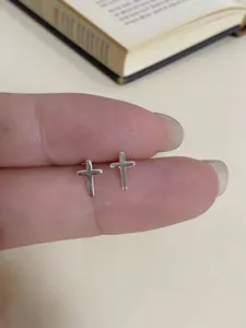 Close-up of minimalist tiny silver cross stud earrings held between fingers for scale
