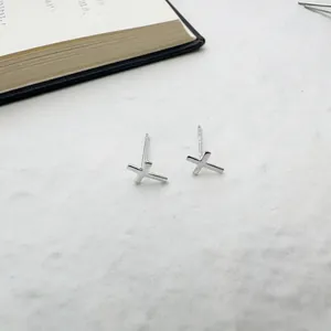 Polished S925 sterling silver mini cross stud earrings on a white stone background