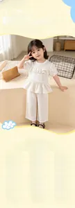 Detail of girls white ruffled short sleeve top and matching wide-leg trousers in airy fabric