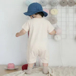 Short sleeve cotton infant romper in beige with back view on a cozy home background