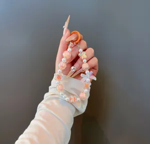 Detail of sweet beaded keychain with orange bow and clover charm held by hand