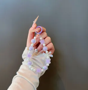 Detail of beaded phone charm with purple petals, pearls, and a large bow decoration
