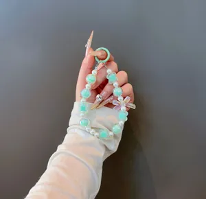 Handheld view of a sweet beaded charm with mint green bow and clover details